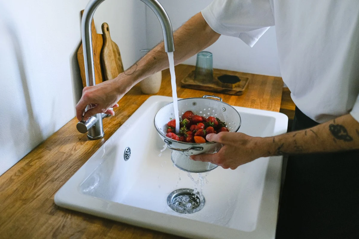 Strawberries rinsed in a colander at a sink