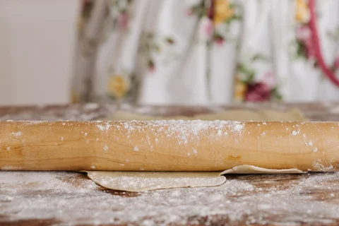 A wooden rolling pin working dough on a floured surface